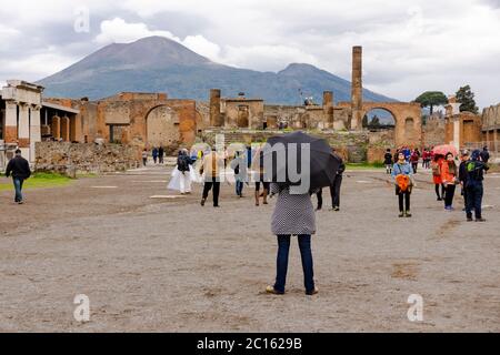 Turistas en un día lluvioso con sombrillas en el Foro Romano (Foro Civile di Pompeya) en la histórica ciudad de Pompeya con el Monte Vesubio detrás, Italia Foto de stock