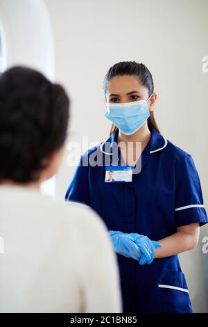 Enfermera con máscara de PPE y guantes hablando con el paciente Foto de stock