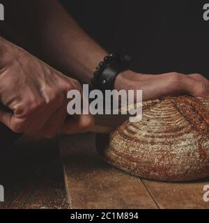 el hombre corta un pan oscuro redondo Foto de stock