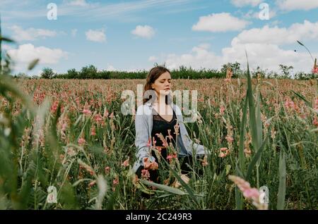 Mujer joven sentada cruz con piernas en meditación en un campo de flores en la vista frontal de la flor