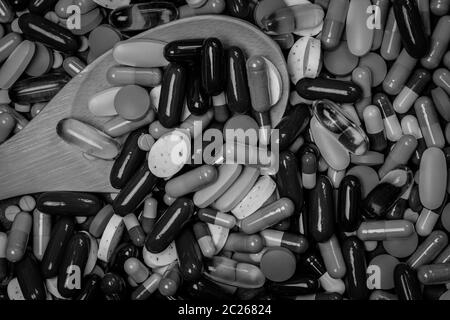 Muchas de las tabletas y las cápsulas de las píldoras y cuchara de madera en la fotografía en blanco y negro. Uso excesivo de drogas y sobredosis concepto. El uso de medicamentos en ancianos con cron. Foto de stock
