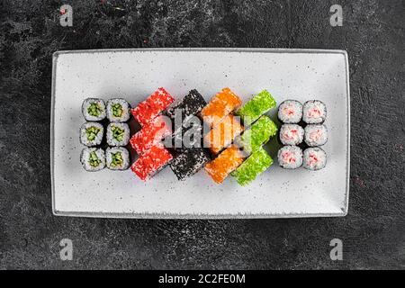 conjunto de rollos y sushi en un plato blanco sobre fondo negro con textura decorado con salsa de soja y especias Foto de stock