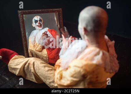  Retrato de scary sangrienta con ojos de payaso loco sentado en el espejo, la pesadilla. Hombre con maquillaje en disfraz de carnaval, mad maniac Fotografía de stock
