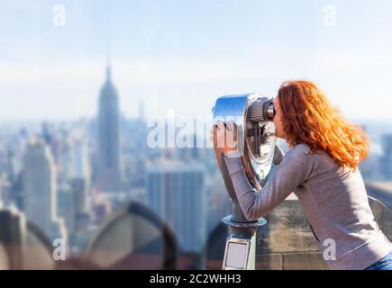 Joven de pelo rojo mirando el panorama de la ciudad en un prismáticos de observación operado con monedas. Foto de stock