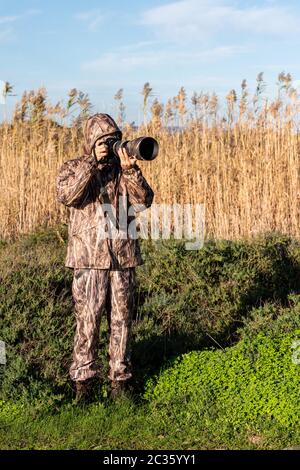 Fotógrafo naturalista en acción, con el camuflaje y la cámara, en el desierto. Foto de stock