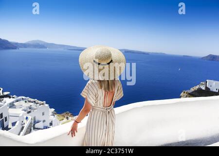 Mujer joven con vestido blanco y sombrero de paja, caminando en la ciudad de Oia, isla de Santorini, Grecia Foto de stock