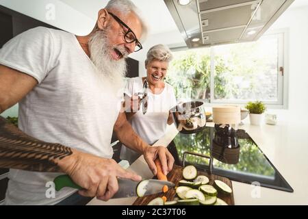 Feliz pareja mayor que se divierte cocinando juntos en casa - ancianos preparando comida de salud en la cocina moderna