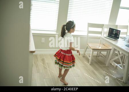 Chica disfruta de una clase de baile en línea con un ordenador portátil conectado a una televisión en casa