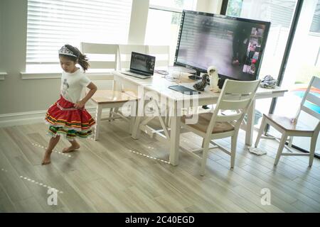 Chica disfruta de una clase de baile en línea con un ordenador portátil conectado a una televisión en casa
