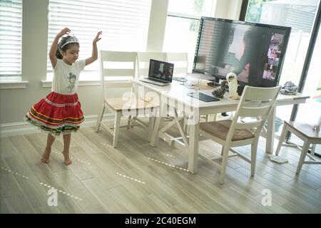 Chica disfruta de una clase de baile en línea con un ordenador portátil conectado a una televisión en casa