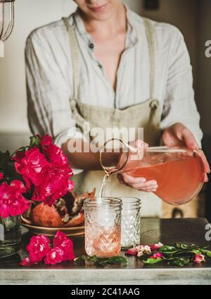 Mujer joven que vierte limonada de rosa a los vasos sobre el mostrador de la cocina