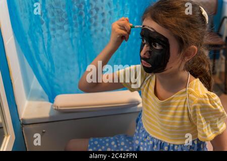 Una niña de una familia pobre y privada se está entreteniendo con pintura de cara Foto de stock