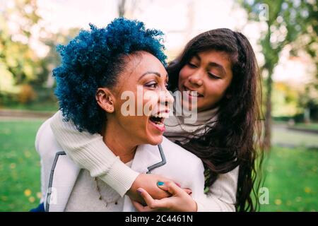Alegre madre riendo mientras que piggybacking hija en el parque