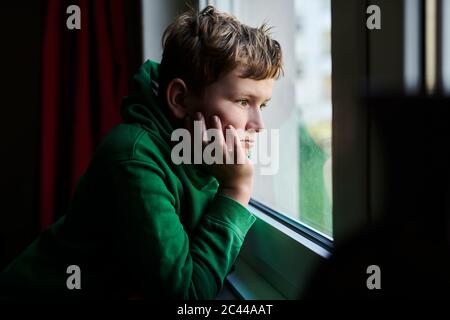 Un niño aburrido mirando a través de la ventana de casa