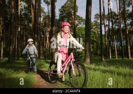 Niña y niño montando bicicletas en el sendero del bosque Foto de stock