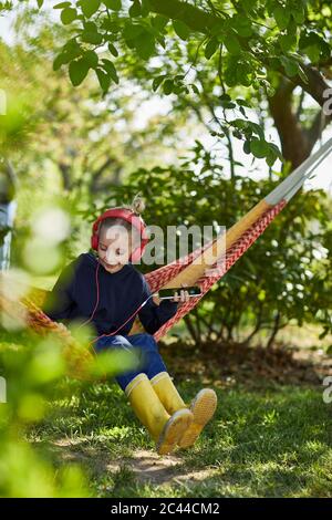 Chica con smartphone y auriculares en hamaca escuchando música Foto de stock