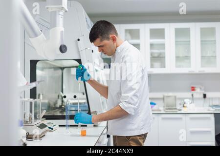 Joven científico masculino tomando químico con pipeta mientras realiza investigaciones en laboratorio