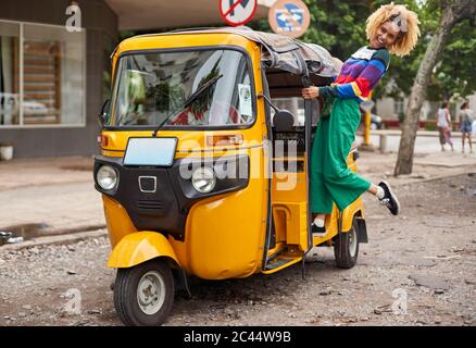 Alegre joven de pie en rickshaw en la ciudad