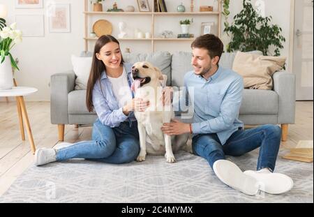 Feliz pareja con perro sentado en la sala de estar