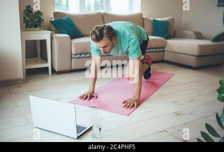 El hombre rubio caucásico con un portátil está haciendo ejercicio fuera de casa en el suelo