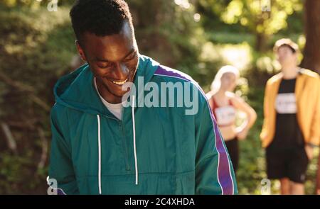 Deportista africano parado en el sendero de montaña mirando hacia abajo y sonriendo con la gente en el fondo.