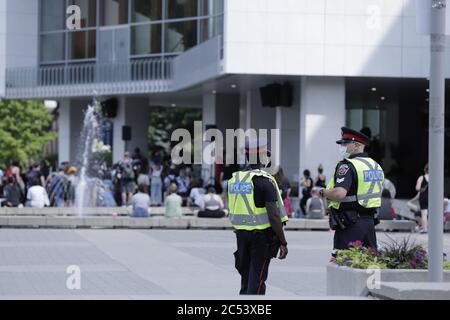 Dos oficiales de policía observan a la gente que se reúne para la protesta pacífica contra el racismo de la BLM en el Hamilton City Hall, Ontario, Canadá Foto de stock
