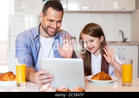 Padre e hija haciendo videollamada tomando el desayuno en casa