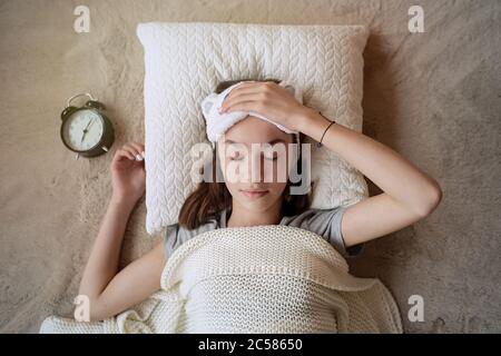 Una adolescente soñolienta que apaga la alarma por la mañana mientras está acostada en la cama