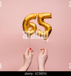 Mano femenina sosteniendo un globo dorado de celebración del aniversario número 65 Foto de stock