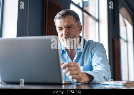 Hombre de negocios maduro trabajando en el portátil. Guapo líder de negocios maduro sentado en una oficina moderna