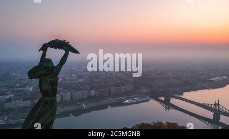 Vista aérea de la Estatua de la Libertad con el Puente de la Libertad y el Río Danubio al fondo tomado de la colina Gellert al amanecer en la niebla en Budapest, Hungría