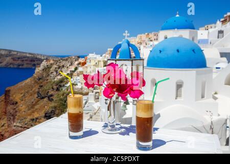 Bebida refrescante y flores en una mesa de madera con el telón de fondo de la isla de Santorini Foto de stock