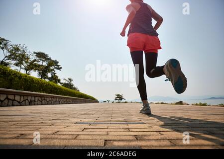 joven mujer adulta asiática corriendo jogging al aire libre, vista trasera y ángulo bajo Foto de stock