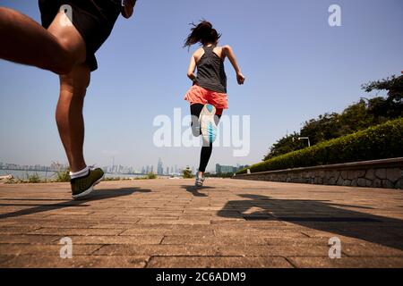 tres jóvenes adultos asiáticos corriendo jogging al aire libre, vista trasera y ángulo bajo