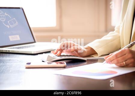 Primer plano de la mano de una empresaria mientras usa la calculadora y escribe algo en el escritorio de la oficina. Foto de stock