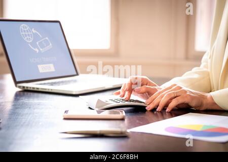Primer plano de la mano de una empresaria mientras se sentaba en el escritorio detrás de su ordenador portátil y utilizaba una calculadora. Foto de stock