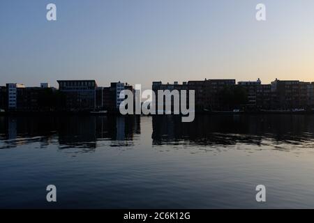 Silueta de edificios modernos en el río IJ en el verano justo antes de la puesta de sol en Amsterdam, Holanda