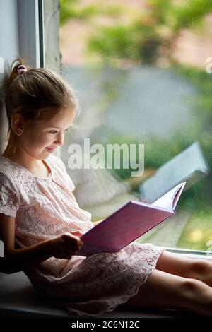Una chica linda leyendo libro en casa, en el alféizar de la ventana