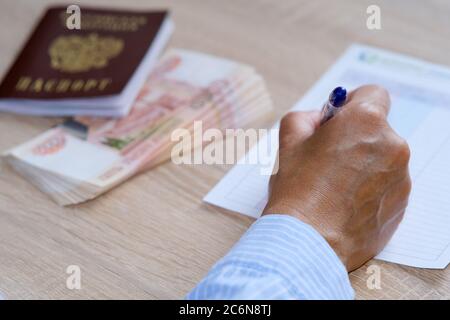 Una persona saca un seguro y pasa una encuesta. Sobre la mesa hay un pasaporte y un paquete de billetes. Foto de stock