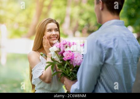 Joven cariñoso sorprendiendo a su novia con ramo de flores afuera Foto de stock