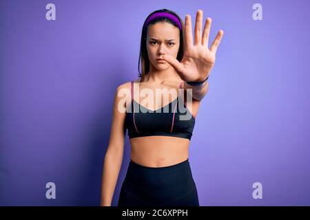 Joven hermosa chica deportiva haciendo deporte usando ropa deportiva sobre  fondo morado aislado haciendo dejar de cantar con la palma de la mano.  Expresión de advertencia w Fotografía de stock - Alamy