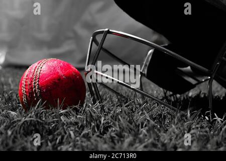 Halmet de cricket y una pelota en una hierba verde. El casco protege al bateador de las bolas rápidas que de otra manera pueden causar daño a la persona que juega.Fotografía en blanco y negro