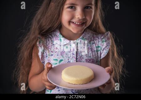 Hermosa niña sorprendida de una sabrosa tarta de queso. Niño listo para comer pastel. Foto de stock
