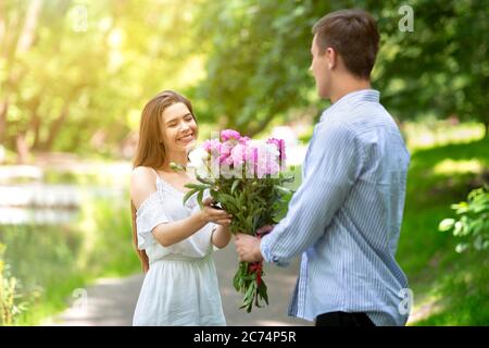 Celebrando aniversario. El joven marido que ama sorprendiendo a su esposa con ramo de flores al aire libre Foto de stock