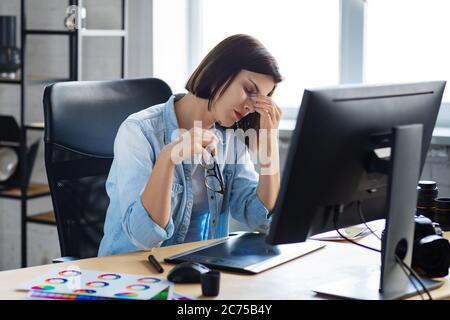 Retrato de un diseñador gráfico cansado trabajando horas extras en la oficina. El trabajador estresado tiene síntomas de fatiga ocular. Retoucher en el lugar de trabajo en el estudio de fotos. Burnout