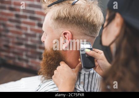El hombre está cortando el pelo en una peluquería. Cuidado del cabello. Barbería en máscara de protección contra virus. Corte de pelo en cuarentena Foto de stock