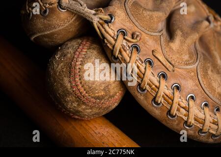 Mitones de béisbol que sostienen un béisbol desgastado encima de un viejo bate rayado. Foto de stock
