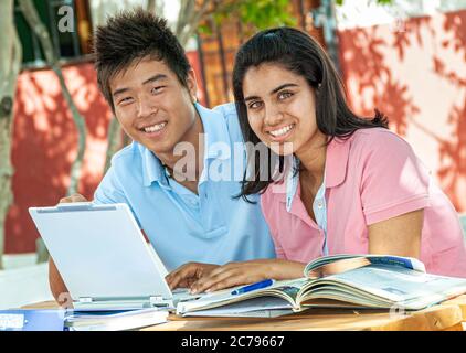 Estudiantes mayores de adolescentes multiculturales Coreano Asiático 15-17 años estudian juntos en una computadora portátil al aire libre en el soleado campus de la escuela Foto de stock