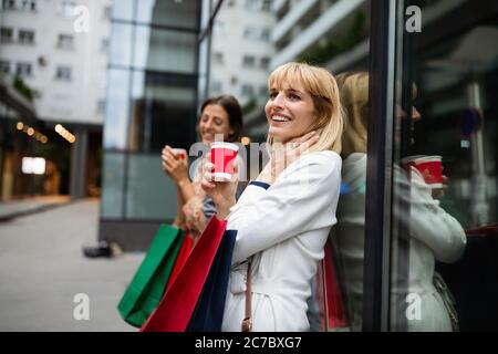Feliz mujer joven bebiendo tomar café y caminar con bolsas después de ir de compras en la ciudad. Foto de stock