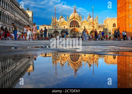 Basílica de San Marco reflejado en acqua alta en la Piazza San Marco al atardecer, Venecia, Italia con movimiento desenfocado en las multitudes de turistas